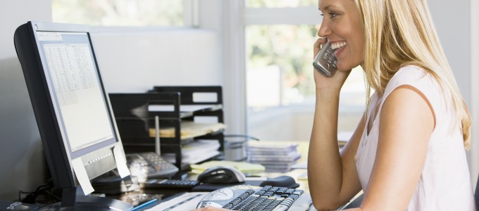 Woman in office with computer using VoIP telephone